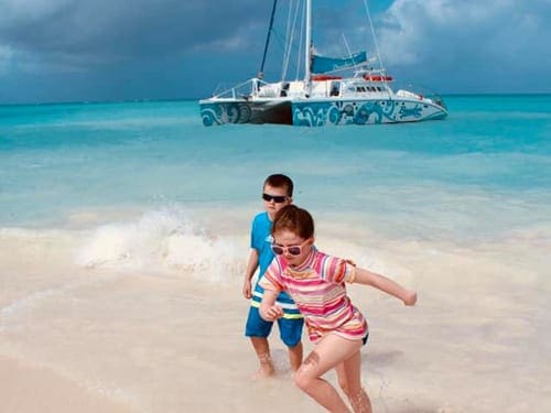 Two kids run along the beack in Turks & Caicos, while a boat rests off-shore.