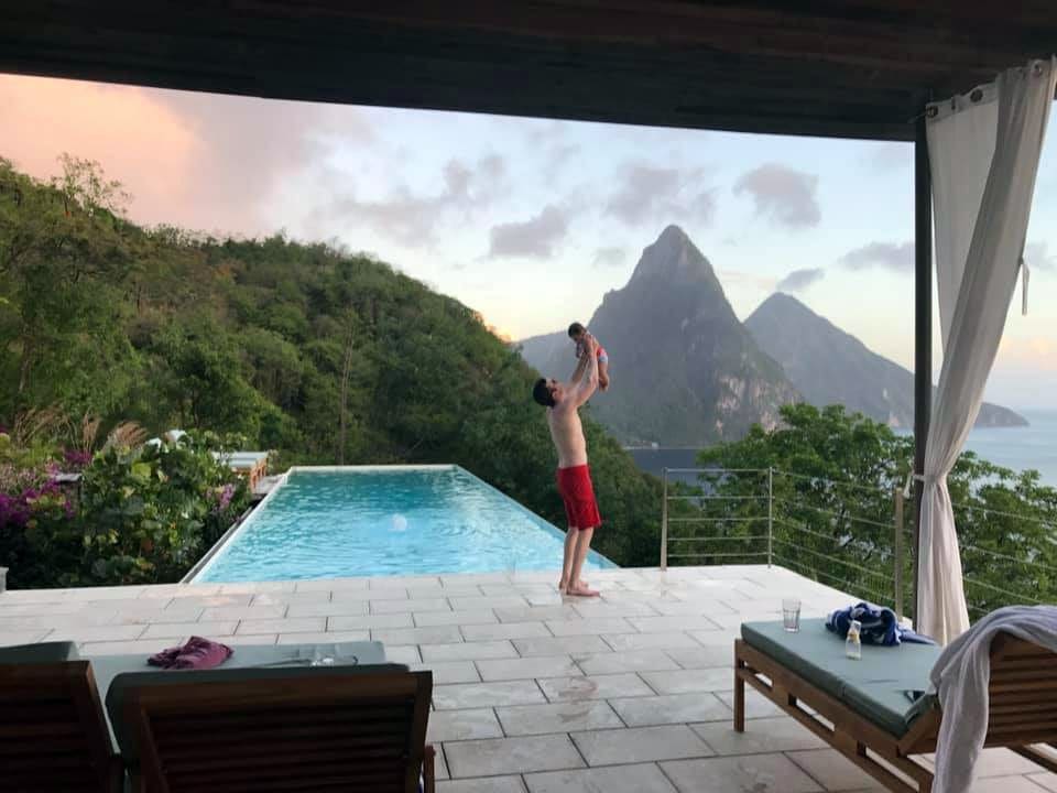 Father holding baby daughter in the air by pool overlooking St. Lucia