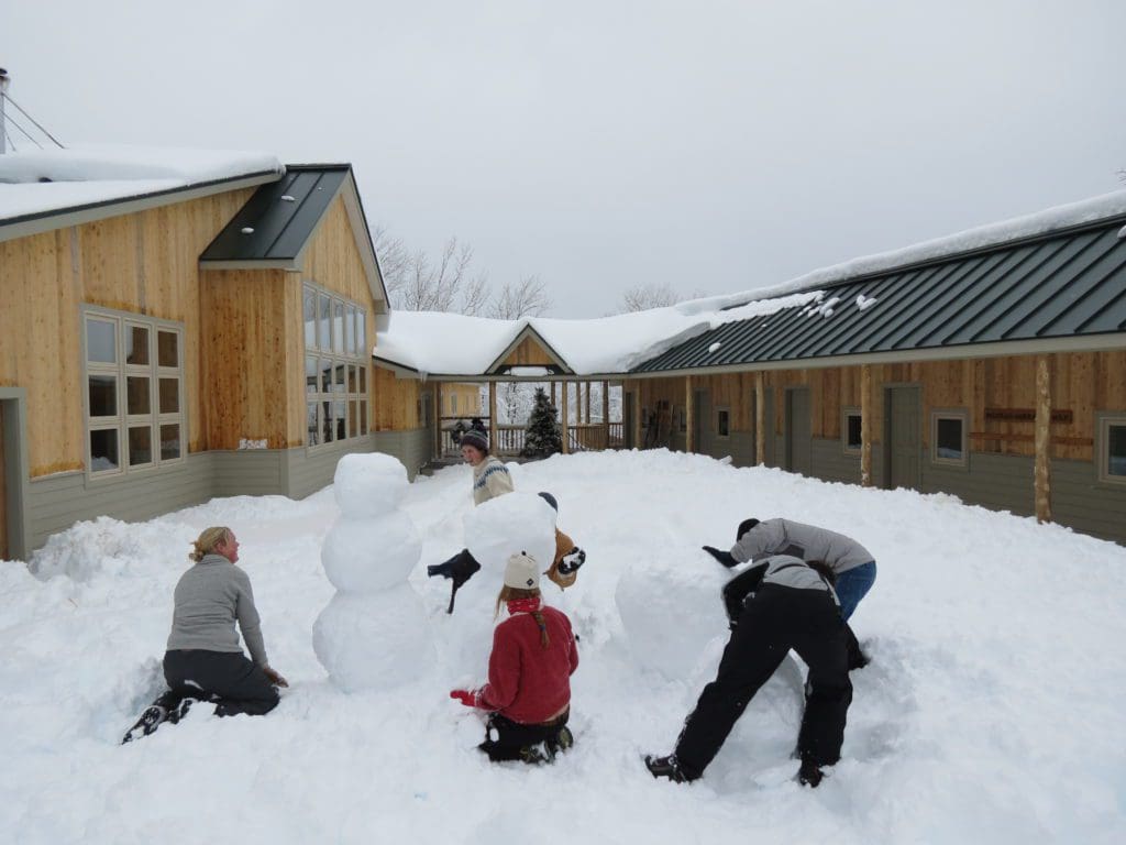 Kids kneeling in the snow and building snowmen at Maine Huts & Trails.