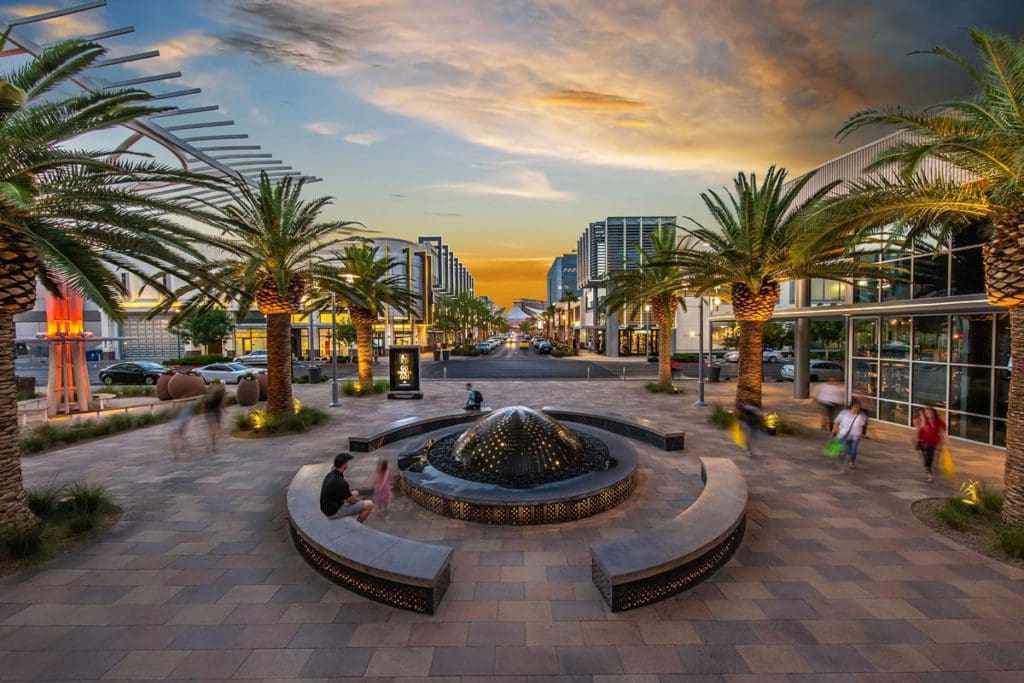 An outdoor patio area in Downtown Summerlin, featuring a small family sitting on centrally located benches at sunset.