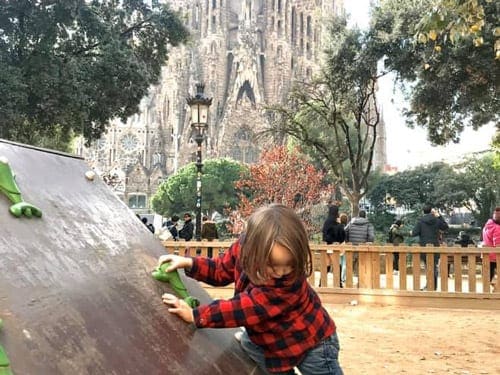 A young boy plays in a Barcelona park, with La Sagrada Familia in the distance.