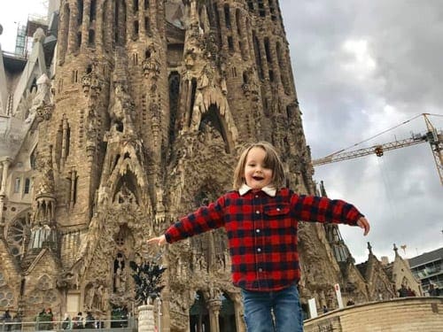 A young boy holds his hands out wide in front of La Sagrada Familia in Barcelona.