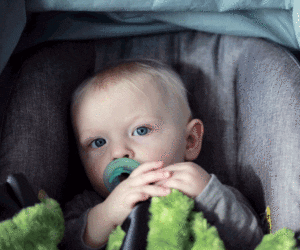 Baby with blue eyes and pacifier sitting in carseat