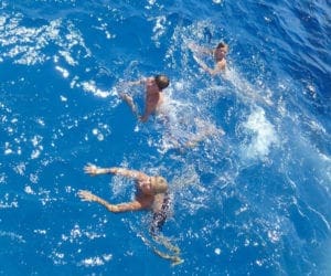 Three children swimming in blue water in Cayman Islands.