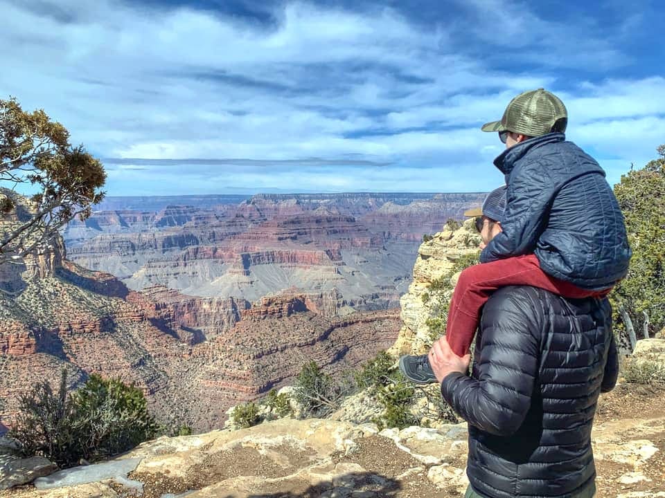 Kid on the dads shoulder in the Grand Canyon, taking in a scenic view.