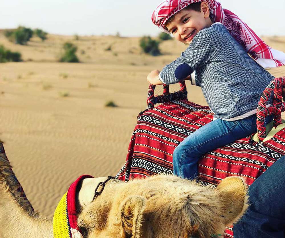 A young boy turns around to smile as he rides a camel in the dessert near Dubai.