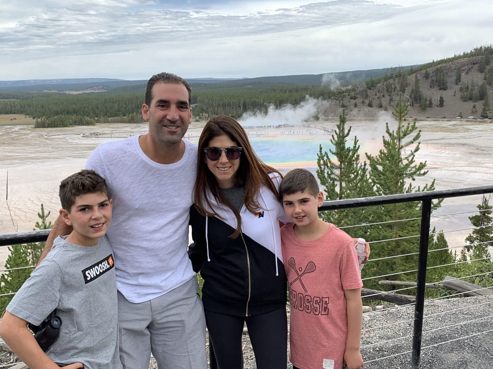 Family in Yellowstone National Park with the infamous rainbow geyser behind them.
