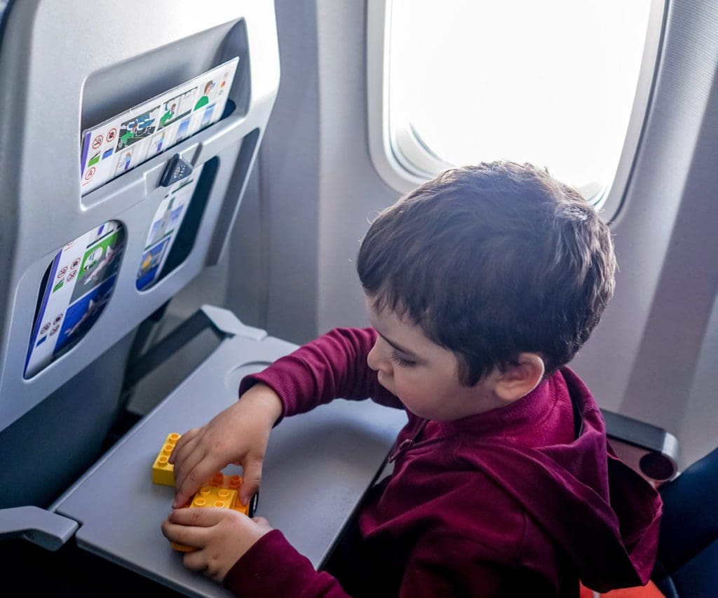 A young boy plays with legos on his airplane tray table during a flight.