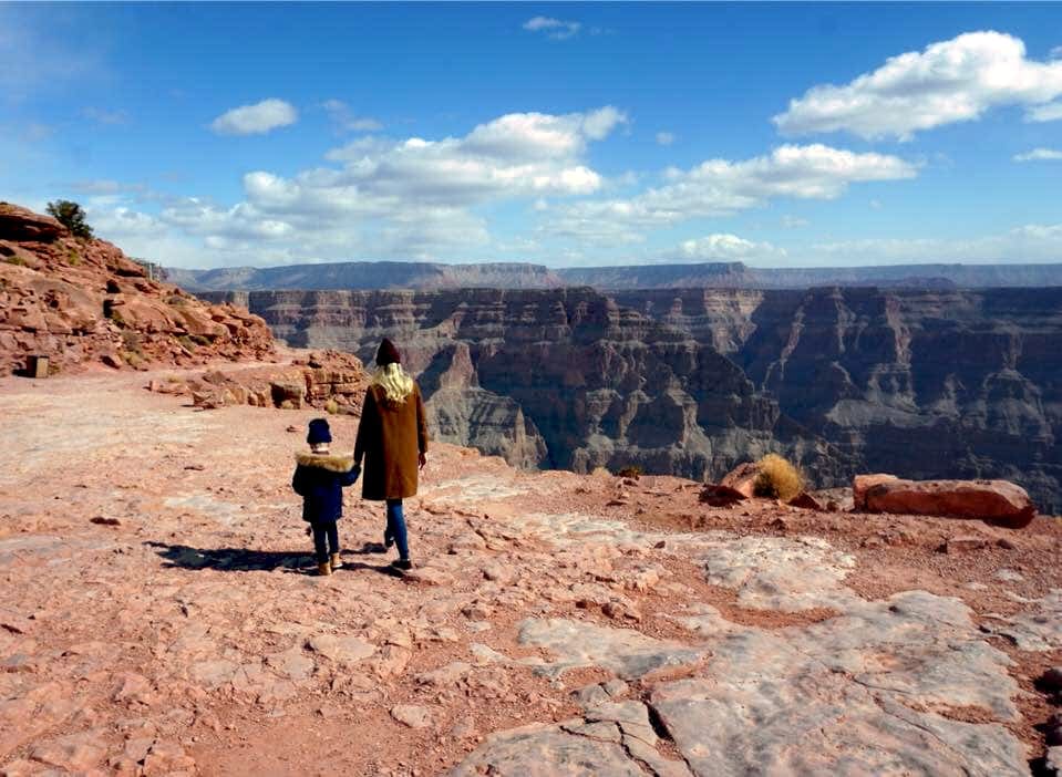 A mom and her young son walk together at the top of the Grand Canyon along the edge.