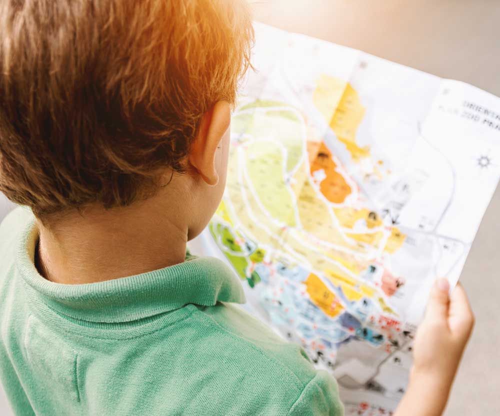 Boy looking at paper travel map. Reviewing the map for your travel plans is one of our tips for traveling with children who have allergies.