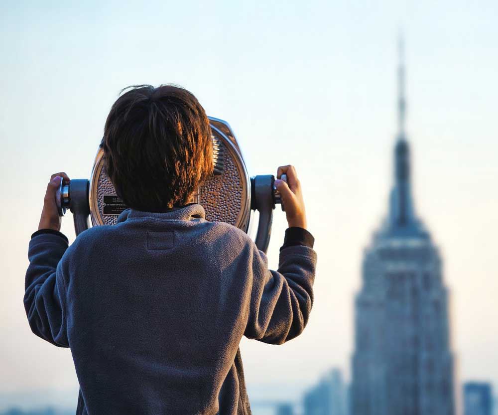 Boy looking at Empire State Building New York through telescope.