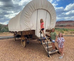 Three kids line up on the stairs about to enter a covered wagon that will serve as their glamping location.