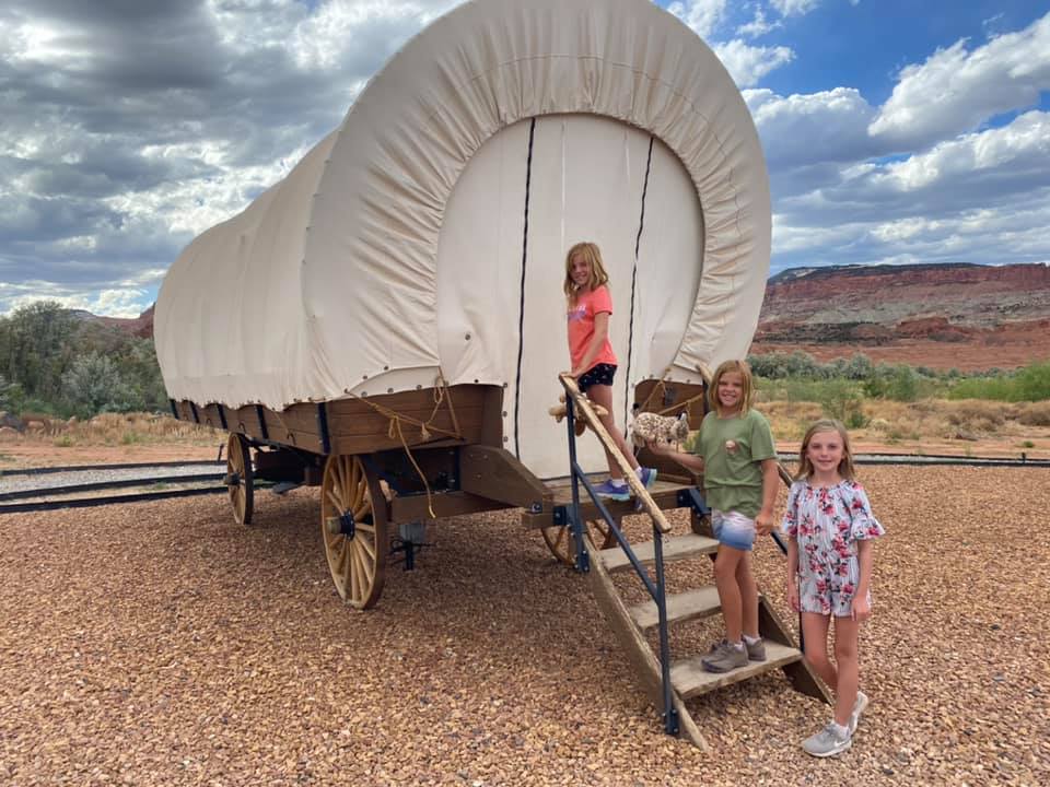Three kids line up on the stairs about to enter a covered wagon that will serve as their glamping location.