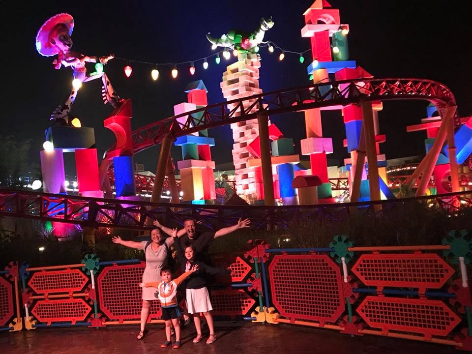 A family of four stands together in front of the decorated Toy Story Land at Hollywood Studios.