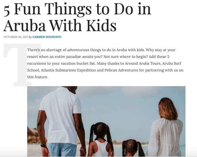 Black family with two girls shown strolling along an Aruba beach as part of the Top FLight Family Blog.