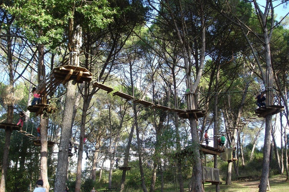 Several people walk across a planked tree-top boardwalk at the Adventure Park in Lisbon, one of the best things to do in Lisbon with kids.