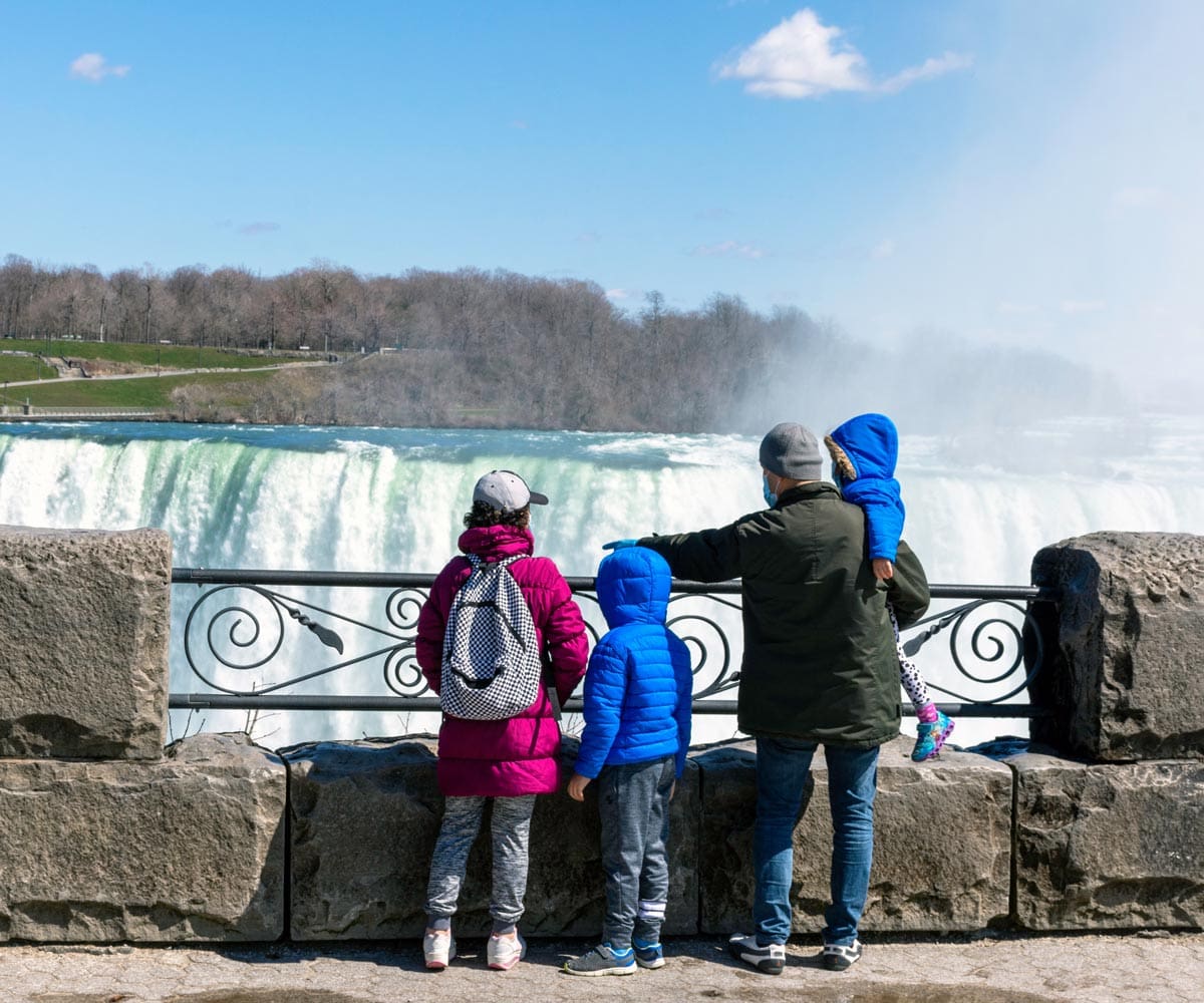 A family of four, all wearing rain coats, stands together looking down on Niagara Falls.