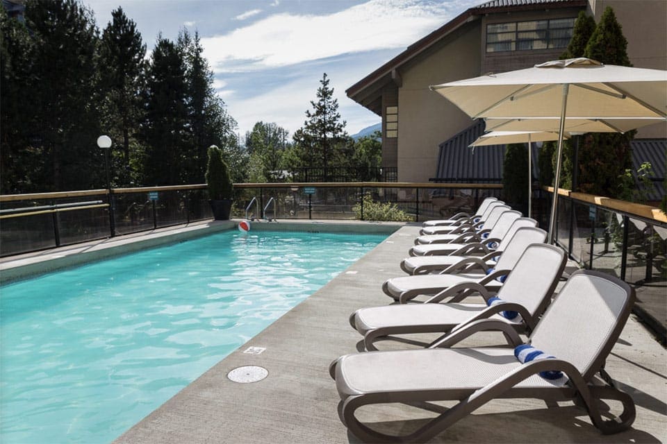 Several pool-side chairs lined along the outdoor pool at Crystal Lodge & Suites, Whistler Hotel.