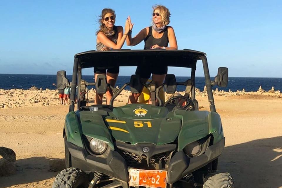 Two women high-five while standing inside a jeep as part of a De Palm Tour, one of the best things to do in Aruba with kids.