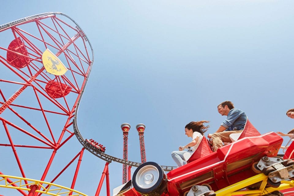 Two adults ride a bright red roller coaster at Ferrari Land.