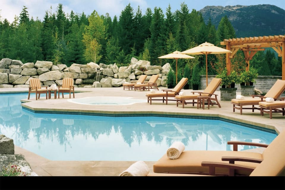 The outdoor pool at Four Seasons Resort Whistler, featuring pines and pool-side chairs.
