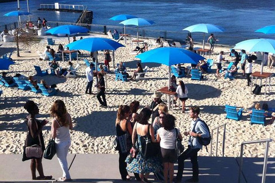 A busy beach, featuring many people and blue umbrellas, at Jacques-Cartier Pier.
