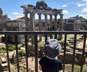 A young child looks through a fence at one of the ancient ruins showcased in the Roman Forum.
