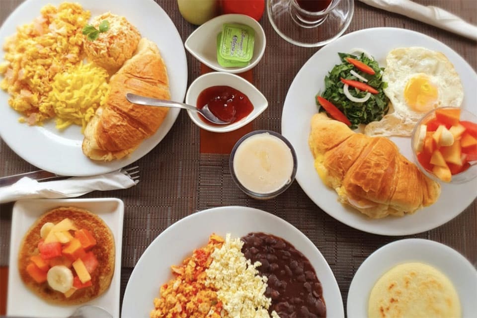 Several dishes from the menu at Kaxapa Factory, one of the best restaurants in Playa del Carmen with kids, including many breakfast items like eggs, croissants, and fruit.