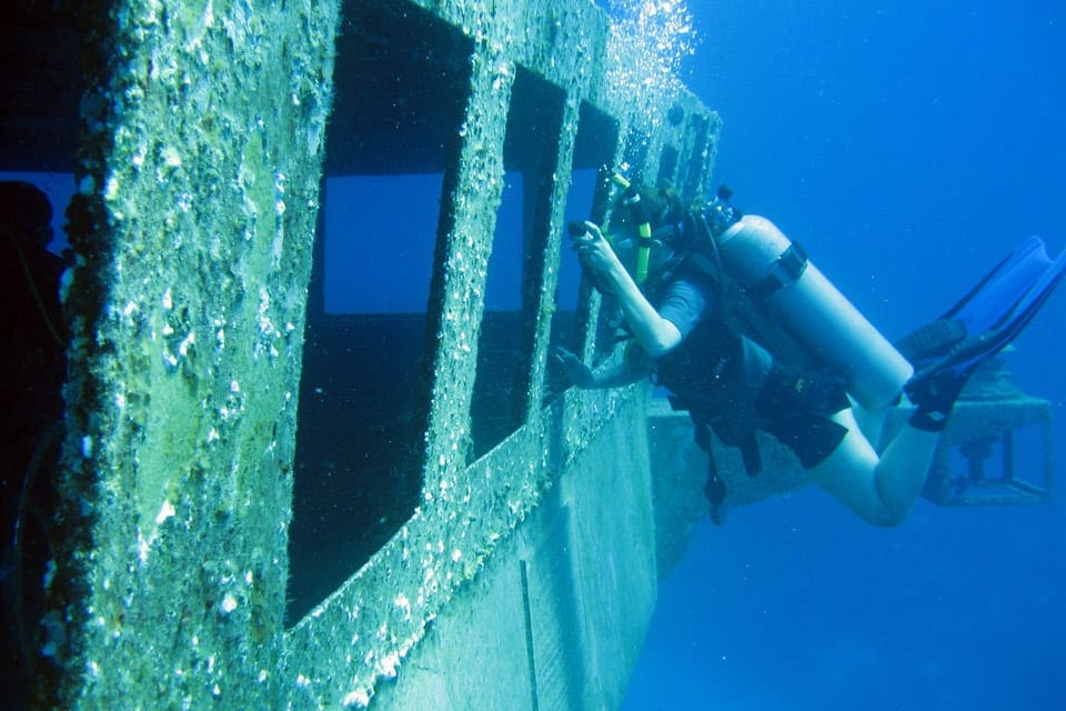 A diver explores a shipwreck through Kittiwake Shipwreck.