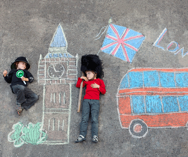 Two kids lay on the cement with chalk drawings of London-inspired things around them, including Big Ben, a flag, and a double-decker bus.