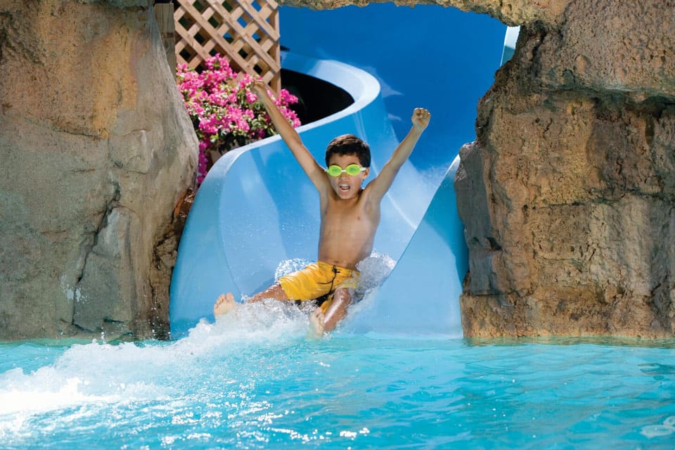 A young boy with his arms in the air goes down a waterslide at Marriott’s Aruba Surf Club.