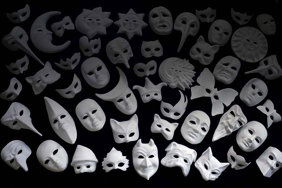 An assortment of white masks on a black table, ready to be painted in a Venice Mask-Making Workshop. 