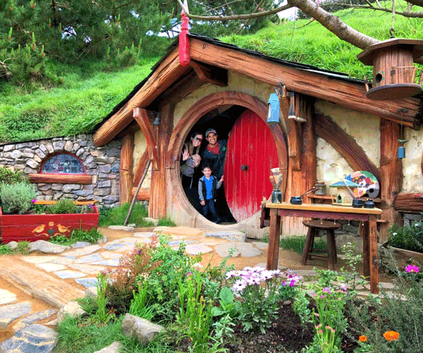 A family of three peeks out of a Hobbiton House.
