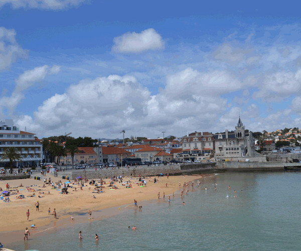 A view of a beach in Portugal, with many beach goers and a city in the background.