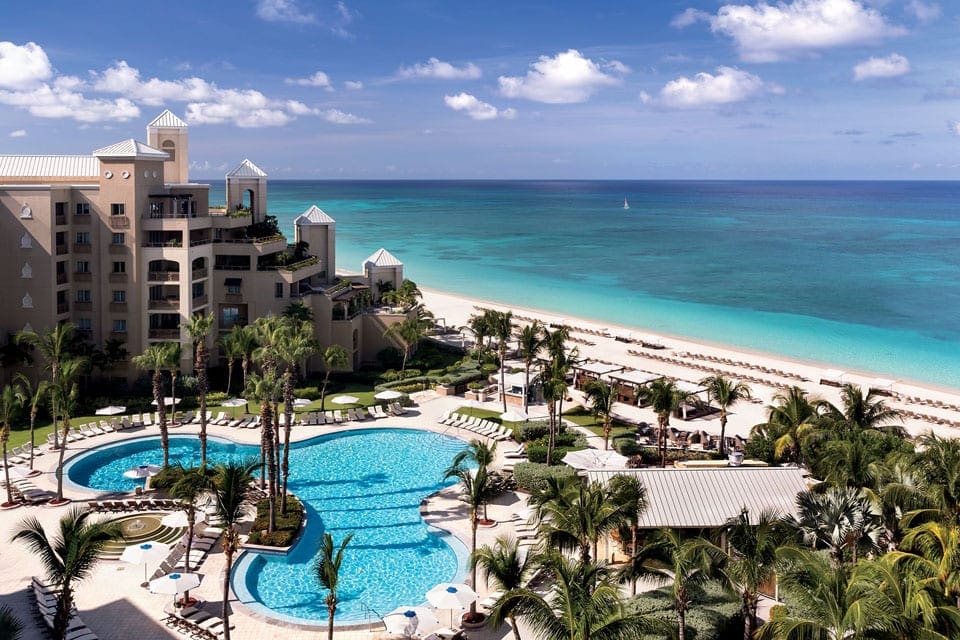 An arial view of the The Ritz-Carlton, Grand Cayman, featuring a large pool, palm trees, and an expansive beach along the property.