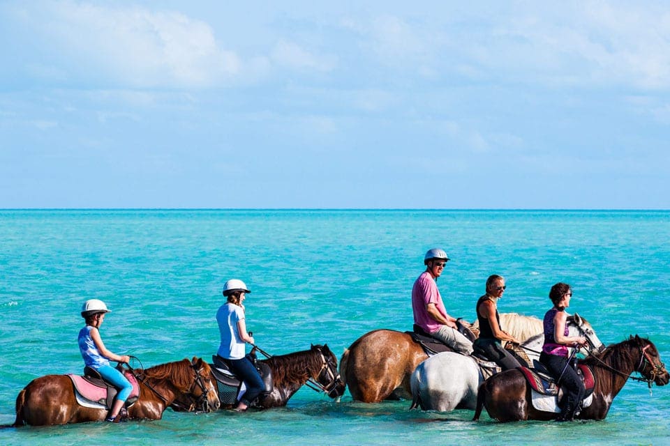 A family of five is horse back riding in the water off-shore while in Turks & Caicos.