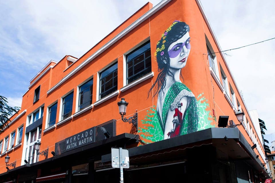 Street art in Madrid, featuring an orange building with a green woman looking backward.