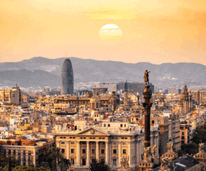 The skyline of Barcelona at dusk, with the sun setting in the distance.