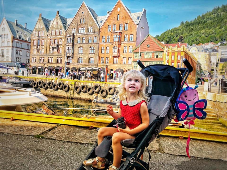 Girl in a stroller in front of a series of buildings in Norway.
