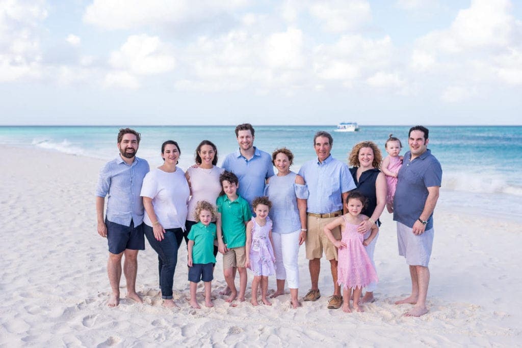 A family of 13 stands on the beach in color coordinating outfits during a family photo shoot in Aruba.