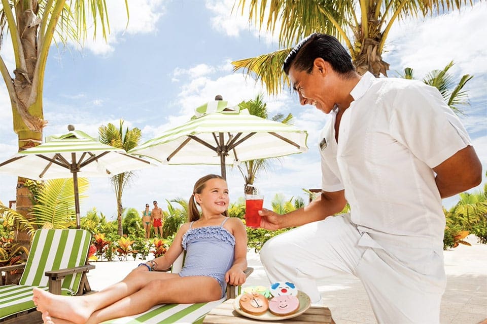 A staff member at Generations Riviera Maya  serves a young child a tropical smoothie and snacks.