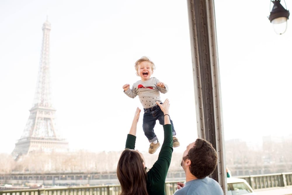 Mother throws young son up in the air in front of the Eiffel tower.