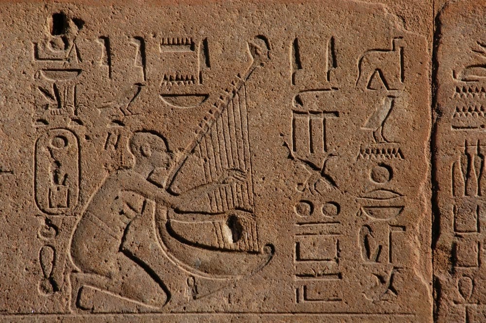 A view of a man playing an instrument in a hieroglyphic dipiction.