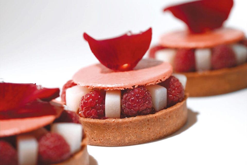 Three delicate desserts, featuring red and white colors, lined up on a plate at Pierre Hermé.