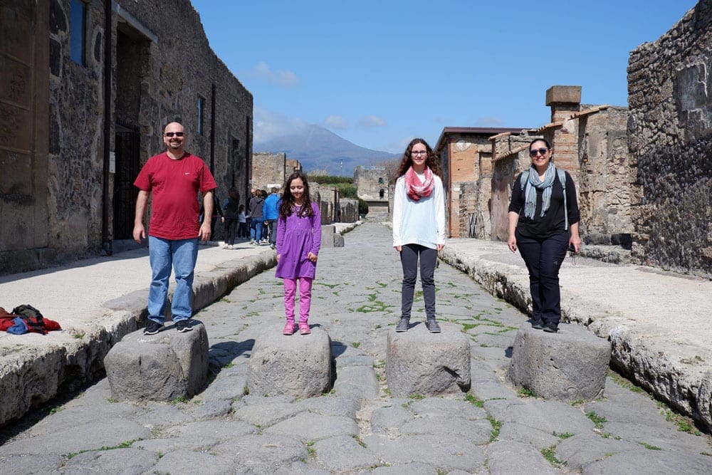 Family of four stands across large rocks in Pompeii. 