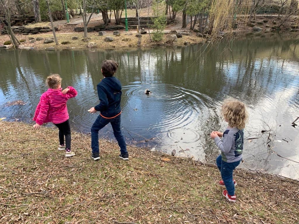 Three kids throw rocks into the water.
