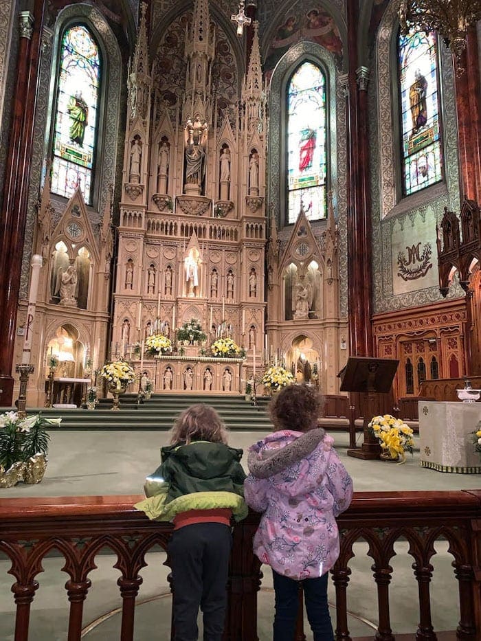 Two kids lean on a railing while enjoying their visit tot he Saint Patrick's Basilica in Montreal.