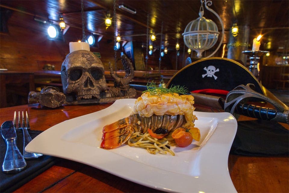 A pirate hat and skull rest behind a lobster dinner aboard a Pirate Dinner Cruise, one of the best things to do in Cancun with kids.