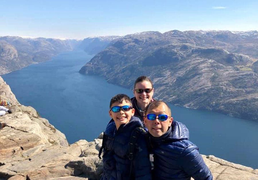 Family of three on a high cliff in front of a Norwegian fjord.