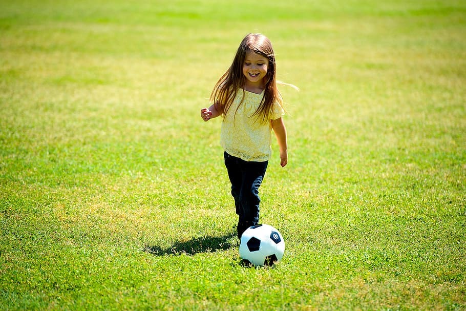 Girl playing soccer in a large green field.